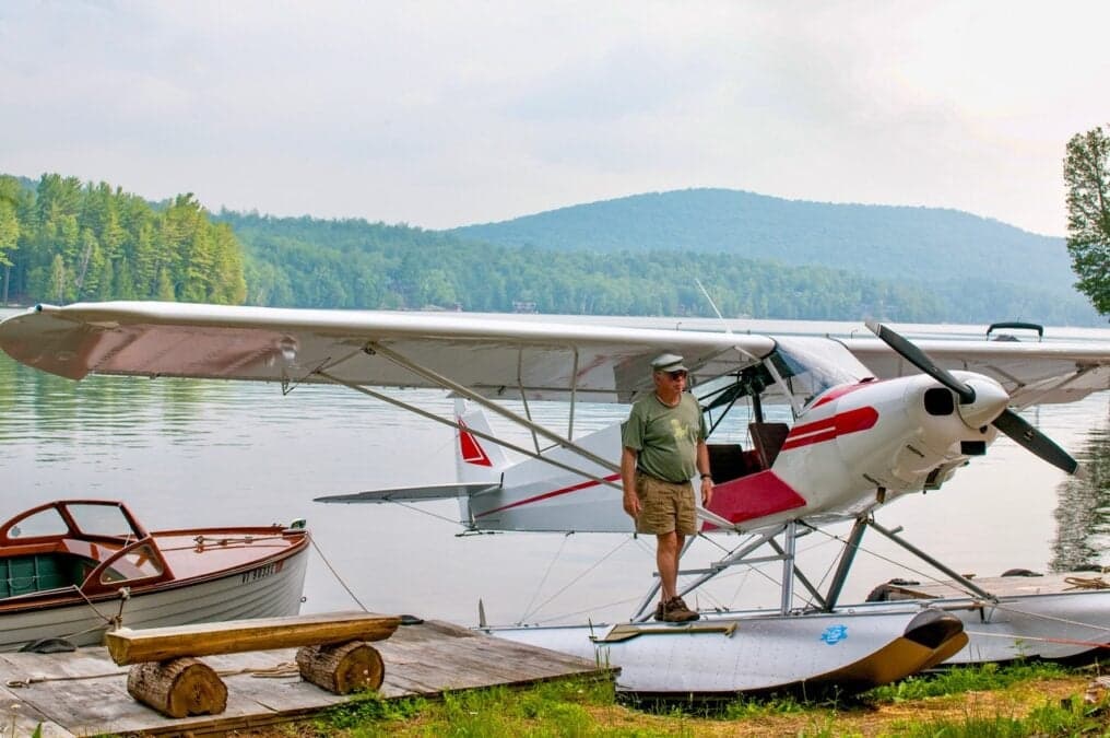 A man stands on the float of a white and red aircraft docked on a lake.
