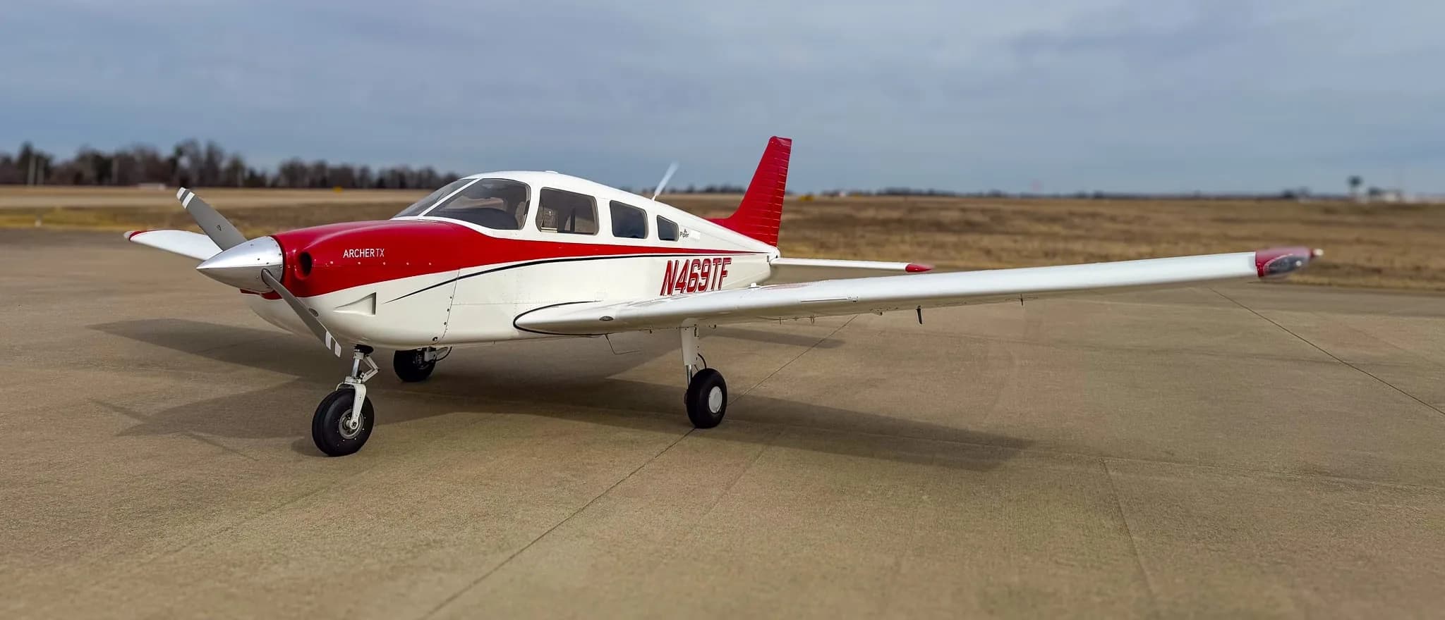 A white and red Piper Archer TX aircraft, N469TF, parked on an airfield under a cloudy sky.