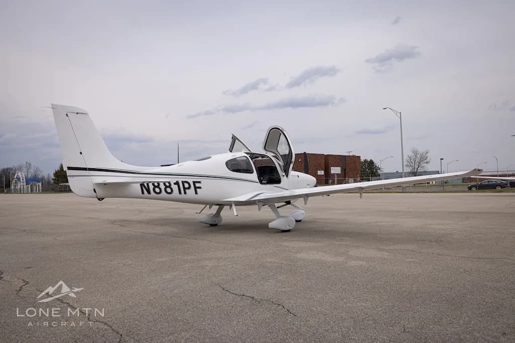 A white Cirrus SR22 aircraft with N881PF registration and open doors, parked on an asphalt ramp with buildings in the background.