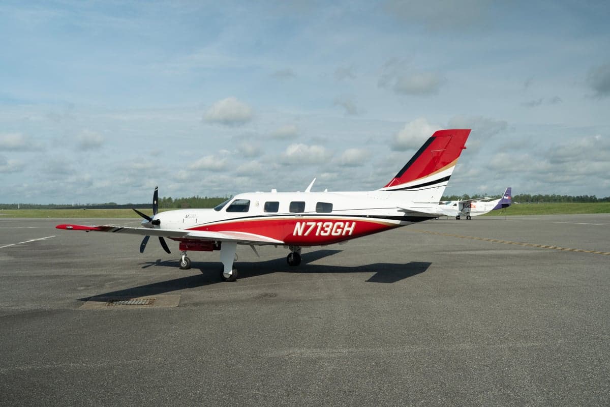 A white and red Piper M500 aircraft with registration N713GH parked on an asphalt tarmac with a FedEx plane in the background.