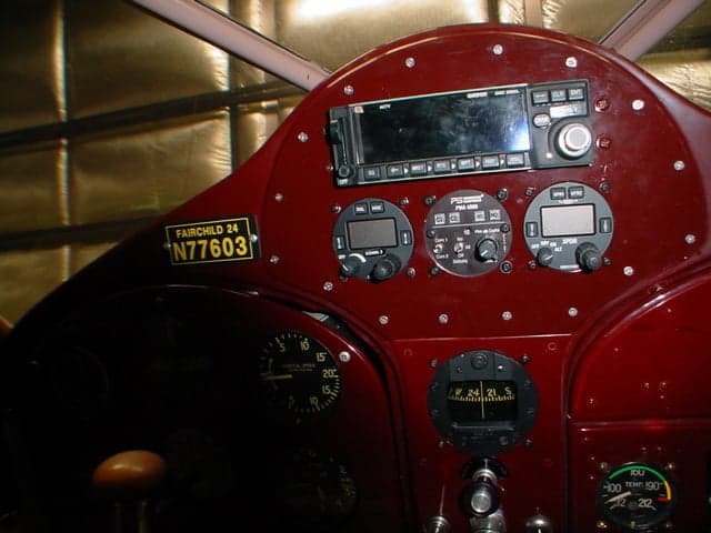 Close-up of the dark red instrument panel of a Fairchild 24 aircraft, showing various gauges and avionics.