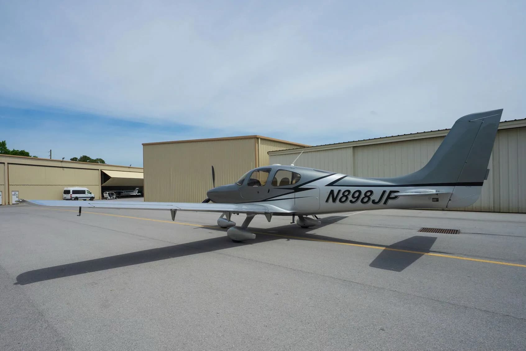 A silver Cirrus SR22 aircraft with black and white accents, registration N898JP, parked on an airfield.