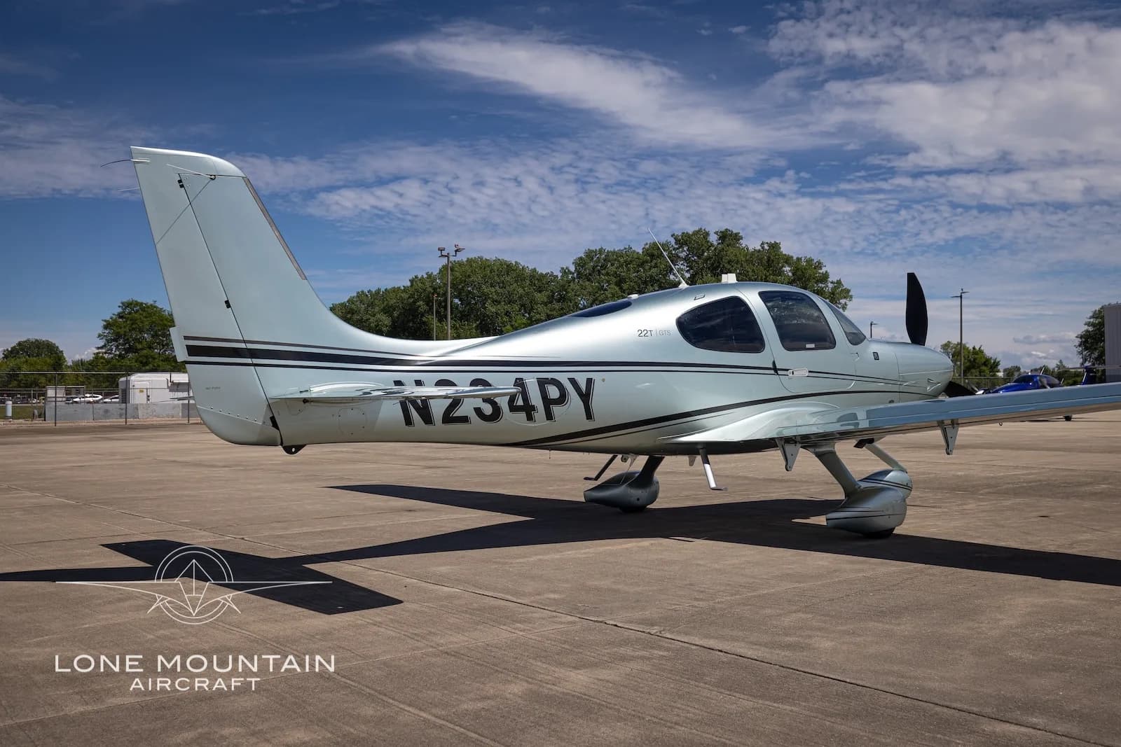 A rear-side view of a silver Cirrus SR22 aircraft (N234PY) with black stripes on a tarmac.