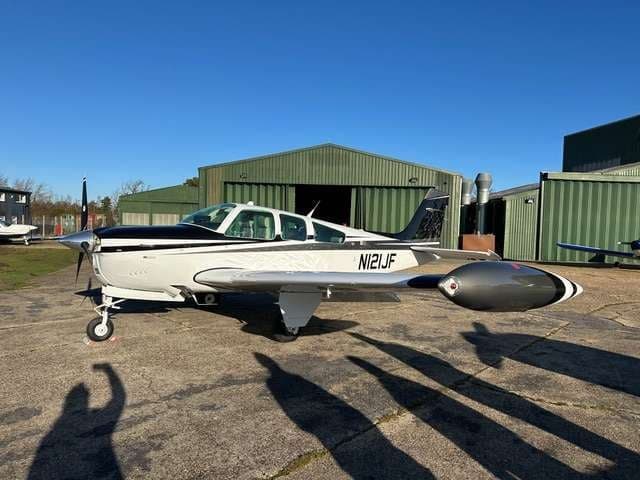 A Beechcraft Bonanza parked on the tarmac with a hangar in the background.