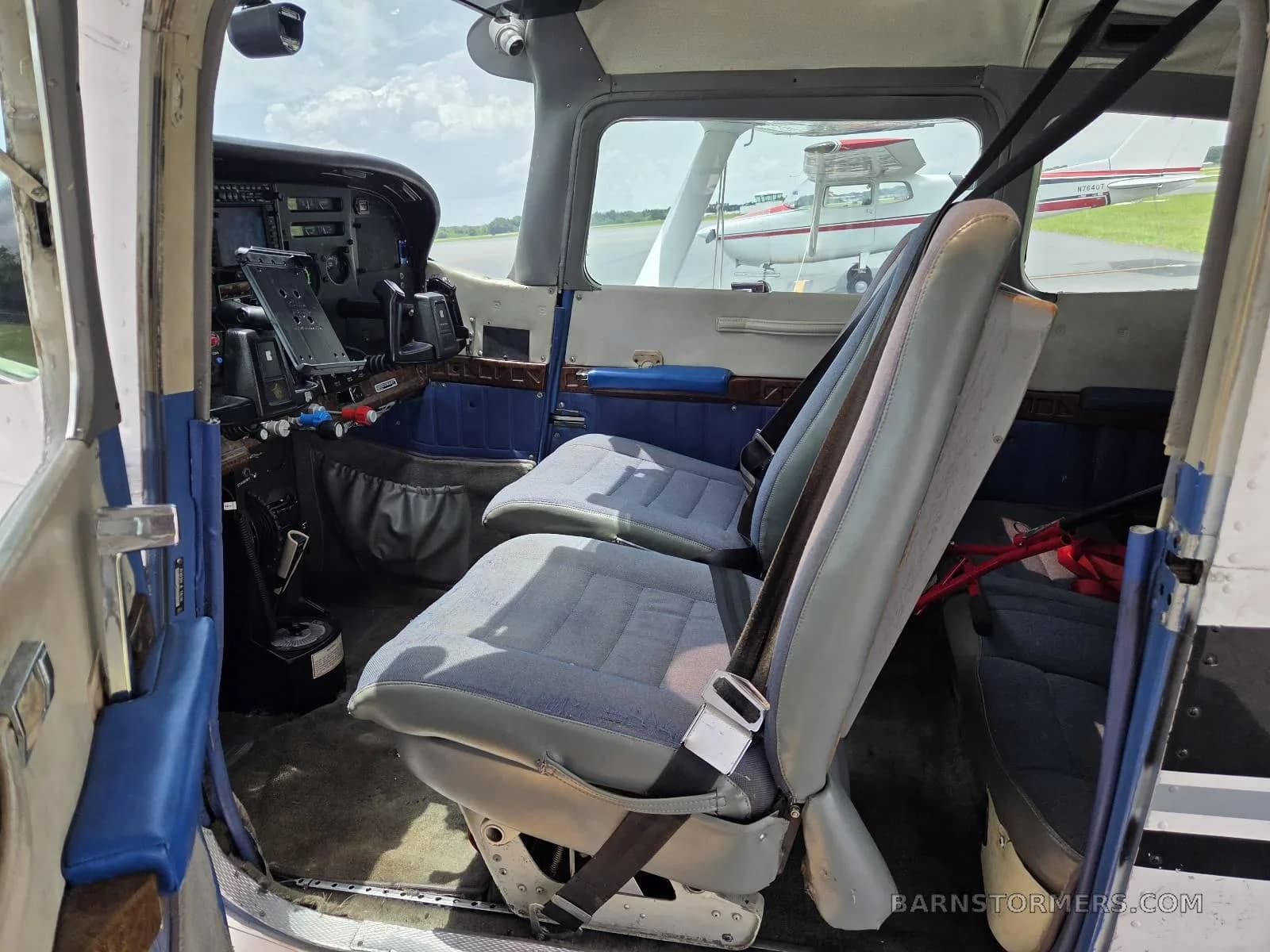 The interior cabin of a Cessna aircraft with blue and gray seats, looking towards the cockpit and an open door.