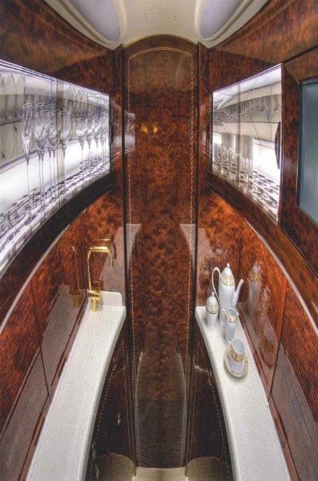 A luxurious aircraft galley or bar area with polished wood, glassware, and a tea set.