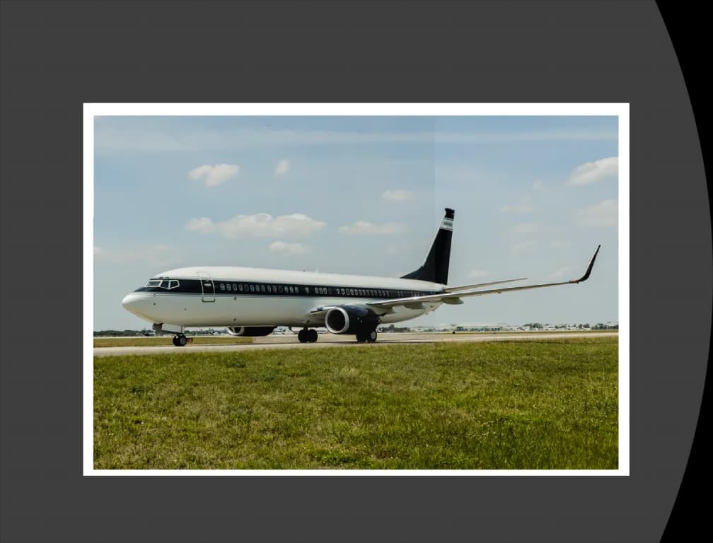 A Boeing 737 BBJ in a dark blue and white livery taxiing on a runway with green grass.