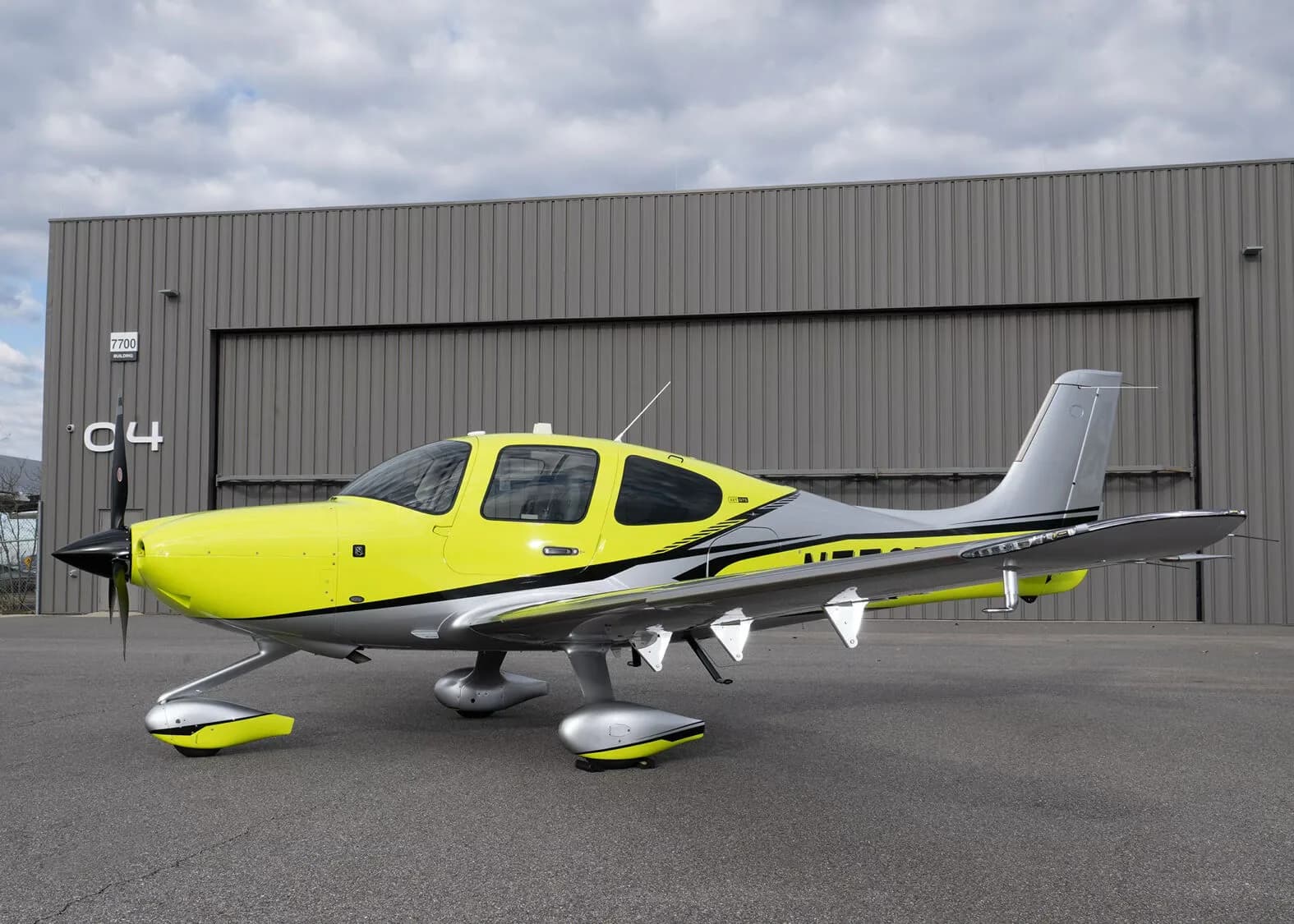 A side view of the yellow and silver Cirrus SR22, N772RG, parked in front of a large grey hangar.