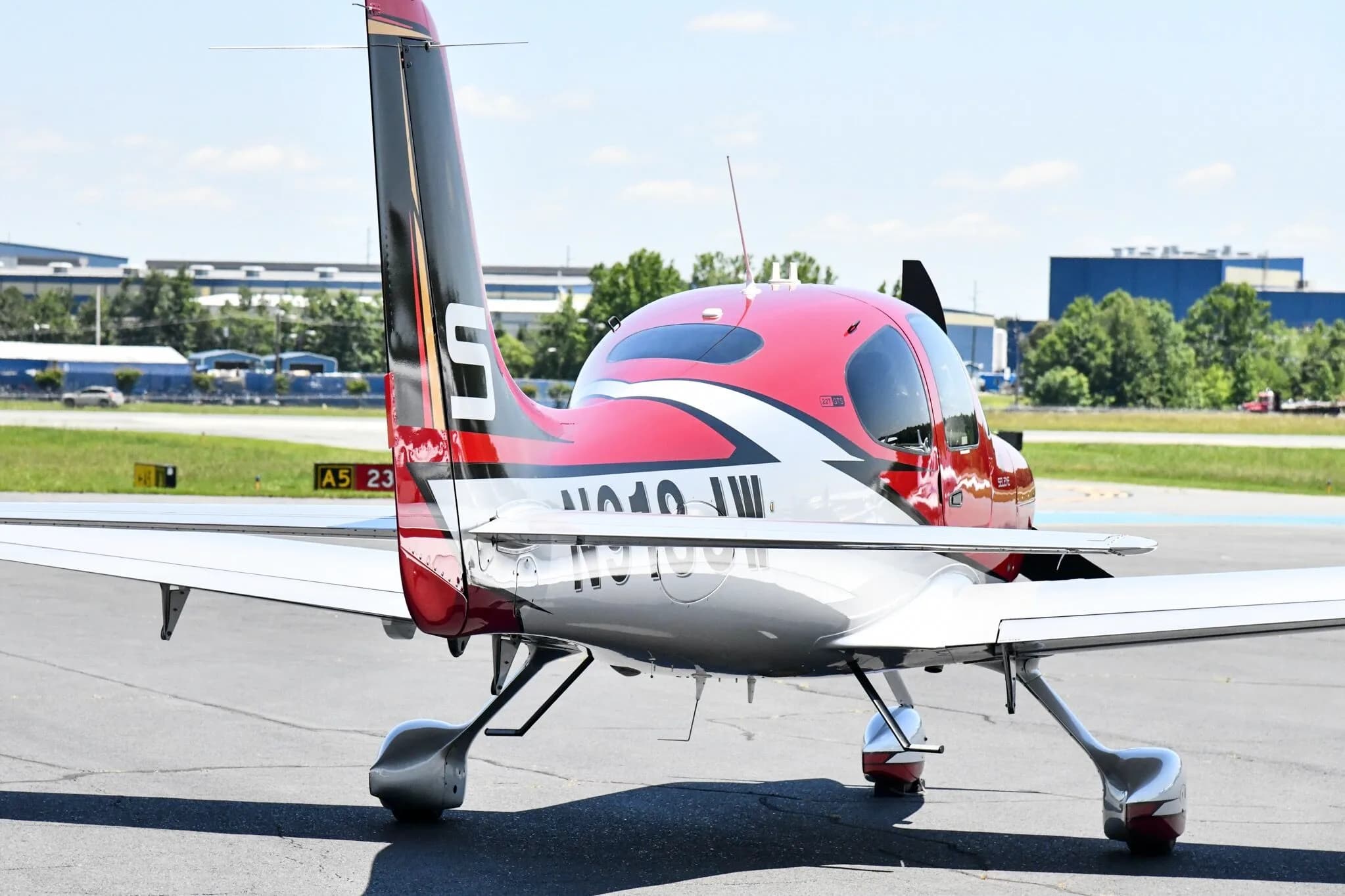 A rear view of a red and white Cirrus SR22T aircraft with registration N918JW parked on an airfield.