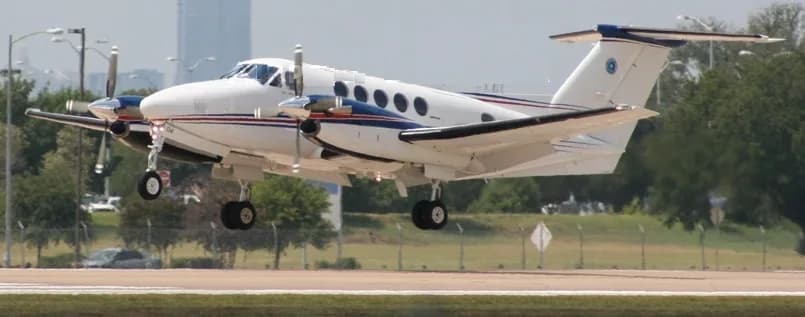 A white turboprop aircraft with blue and red stripes, landing or taking off with its landing gear extended.