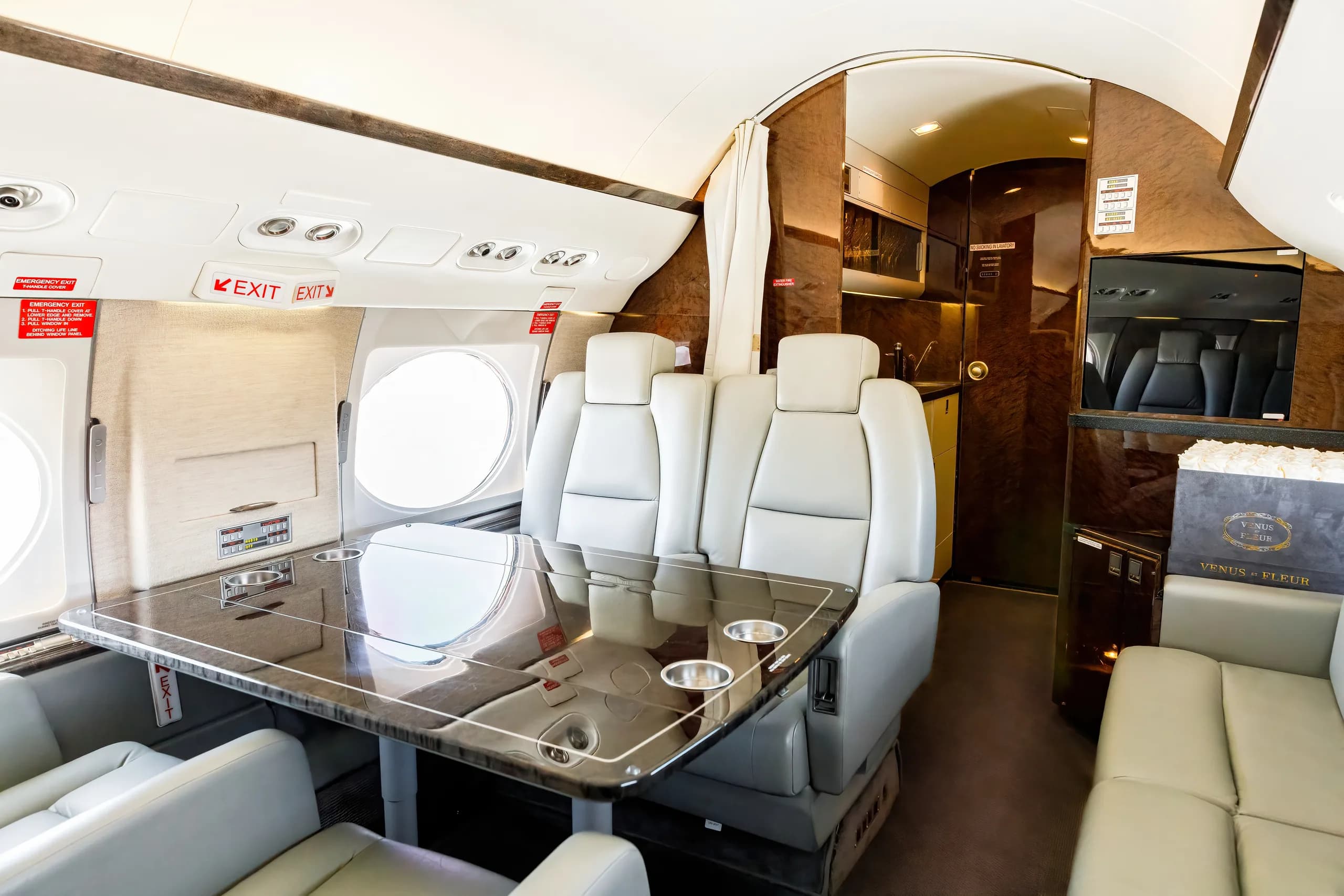 A view inside a private jet cabin shows light gray seats, a dark table with cup holders, and a galley area in the background.