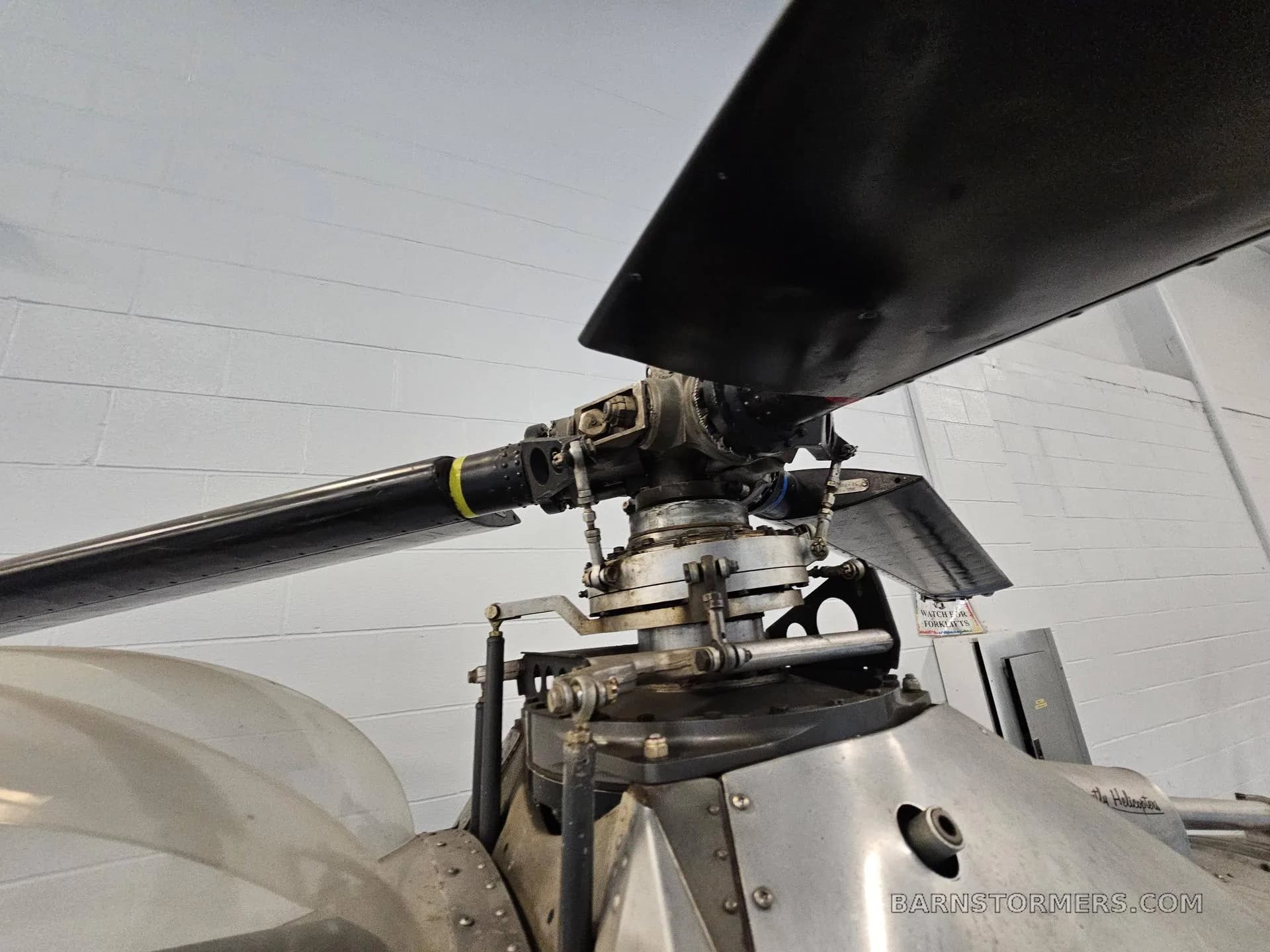 A close-up view of the main rotor hub and blades of a silver helicopter in a hangar.