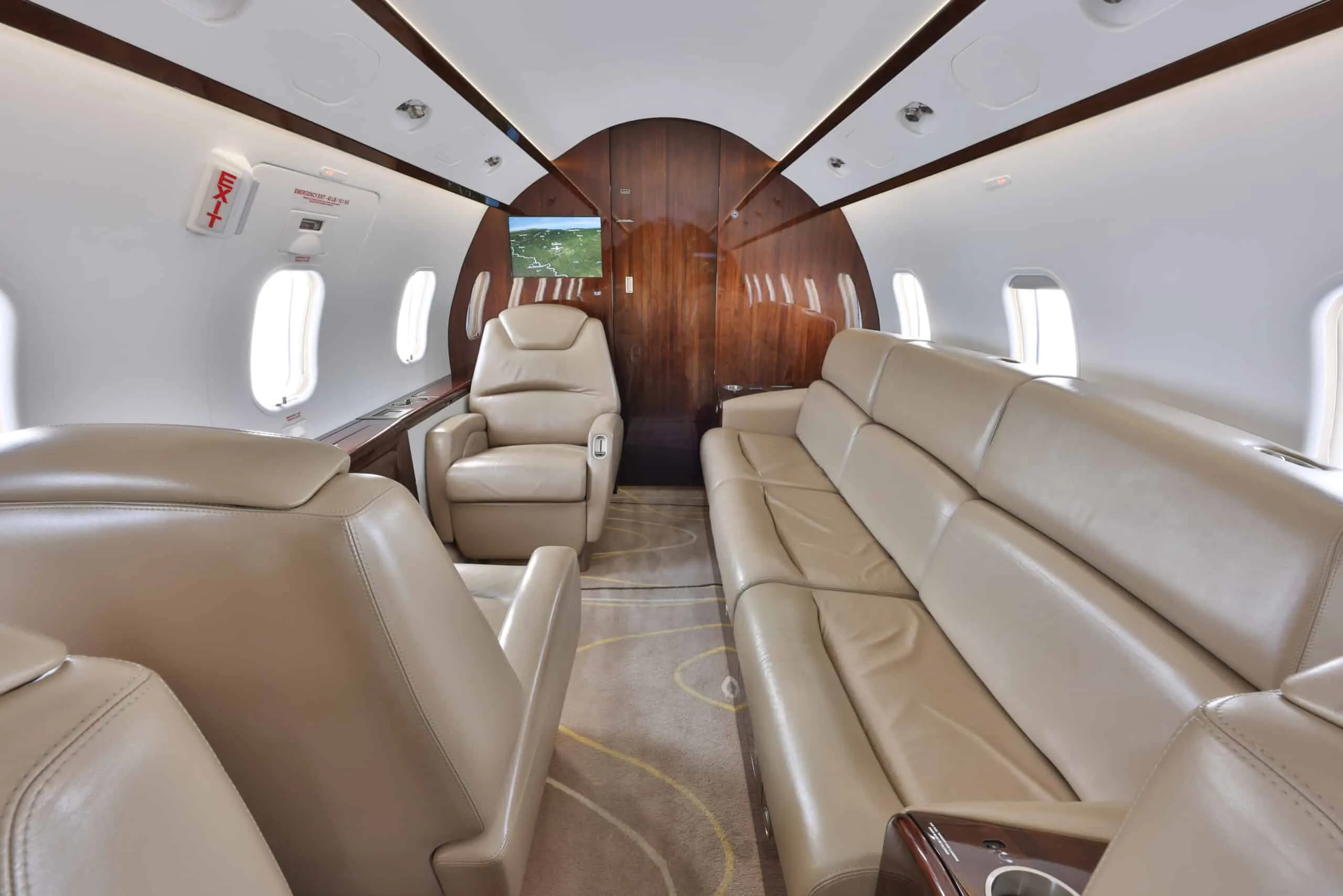 The aft section of a private jet cabin features a beige leather couch and a single club seat.