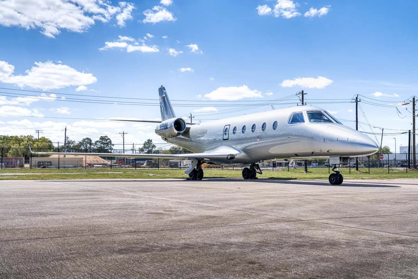 A silver business jet with registration N9MM parked on an airfield, viewed from the front-right.