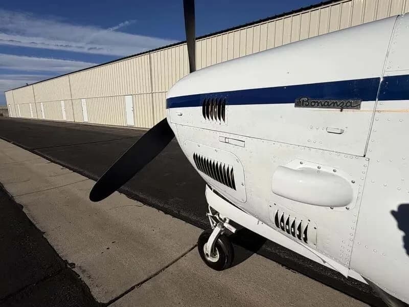 A close-up of the engine cowling and propeller of the white Beechcraft Bonanza, showing the 'Bonanza' script.