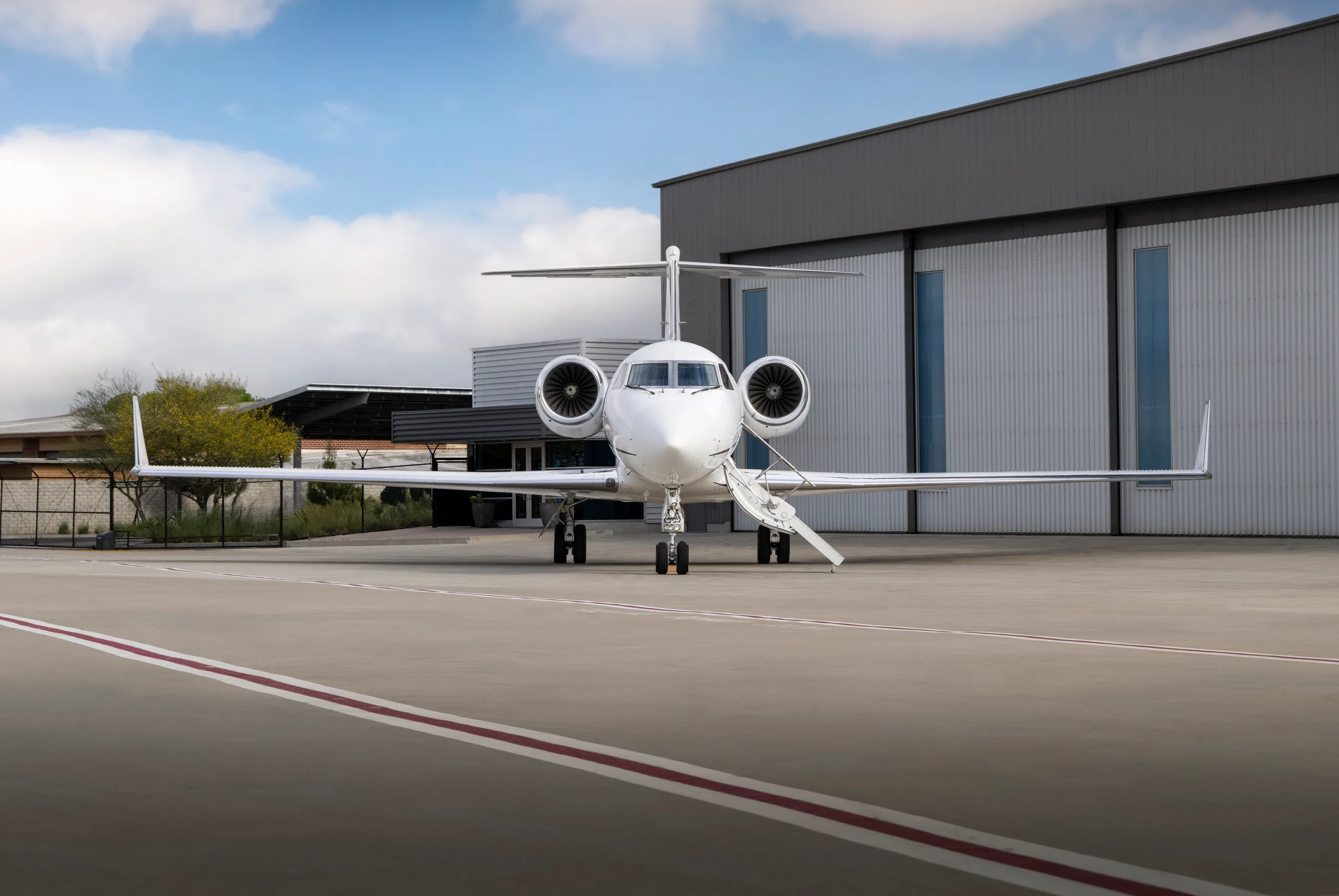 A white Gulfstream G550 business jet parked head-on on the tarmac in front of a hangar.