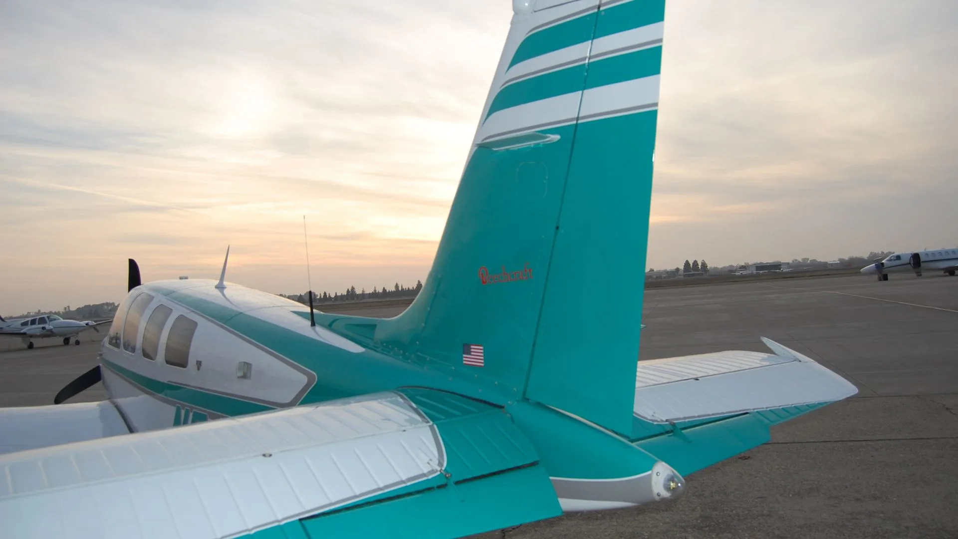 The tail of the Beechcraft Bonanza N54DG, showing the teal and white paint scheme and the Beechcraft logo.