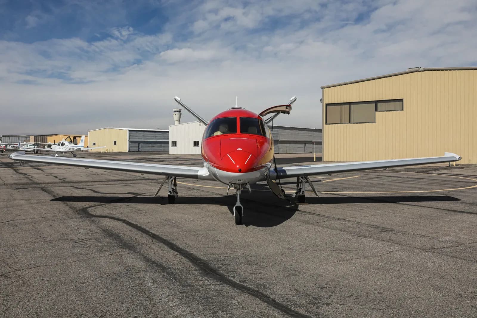 A red and white Cirrus Vision Jet (N1WK) with its doors open, parked on a tarmac, viewed from the front.