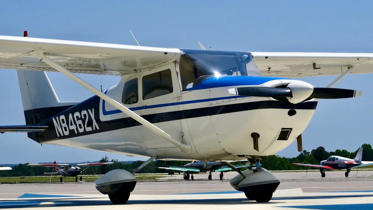 A front-right view of a white Cessna 172 with blue and black stripes, N8462X, parked on an airfield.