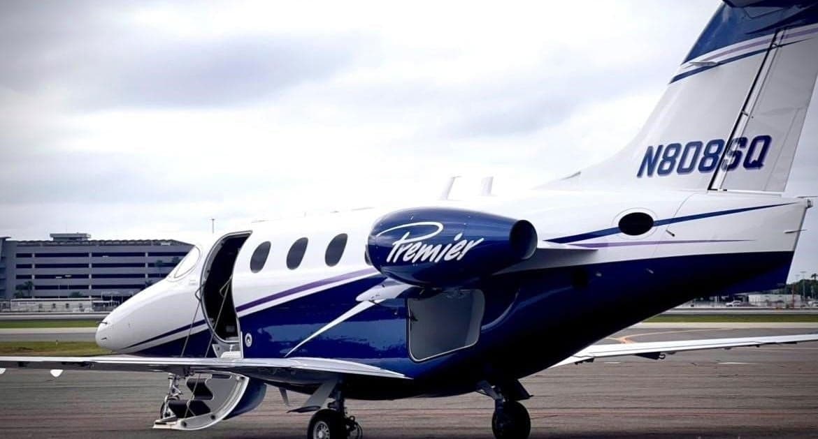 A rear-quarter view of a white and blue Beechcraft Premier 1A jet with registration N808SQ on the tail, parked on an tarmac.