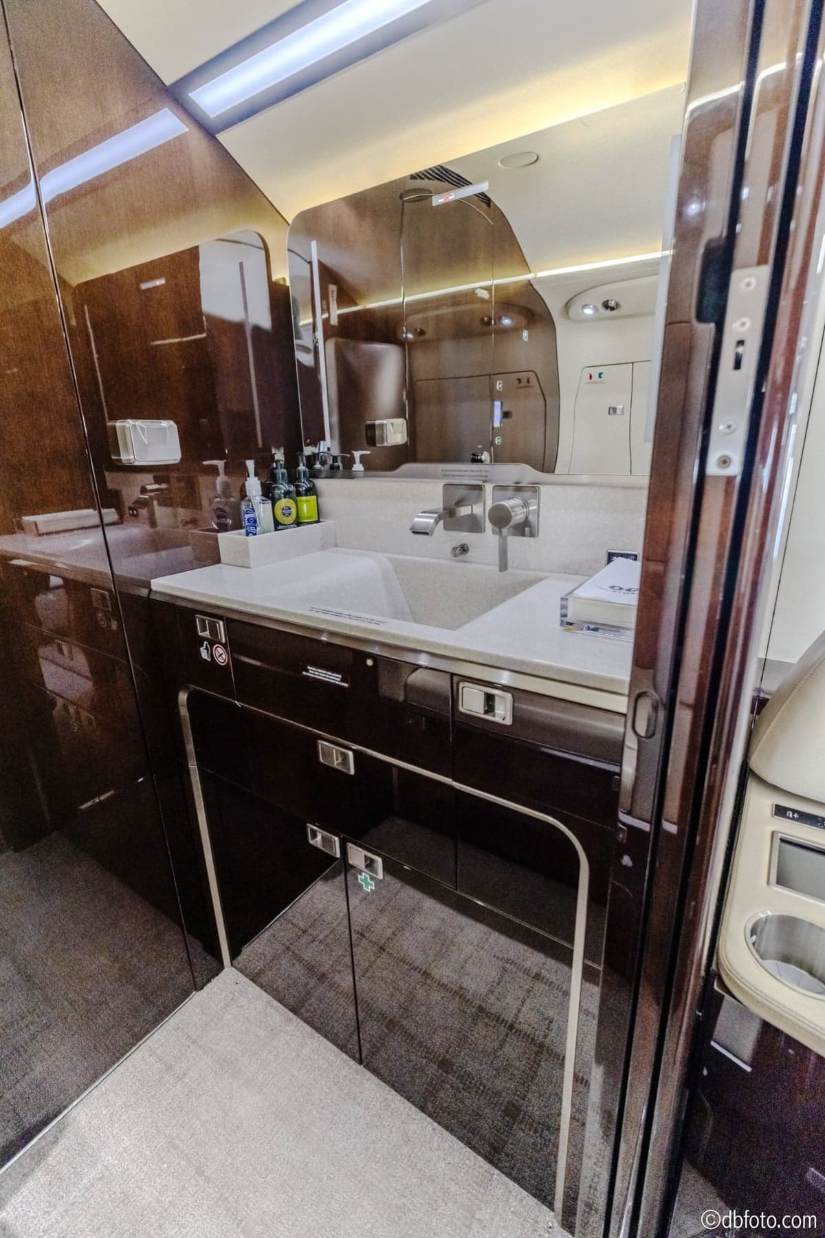 A luxurious aircraft lavatory with a white sink, mirror, and dark wood paneling.