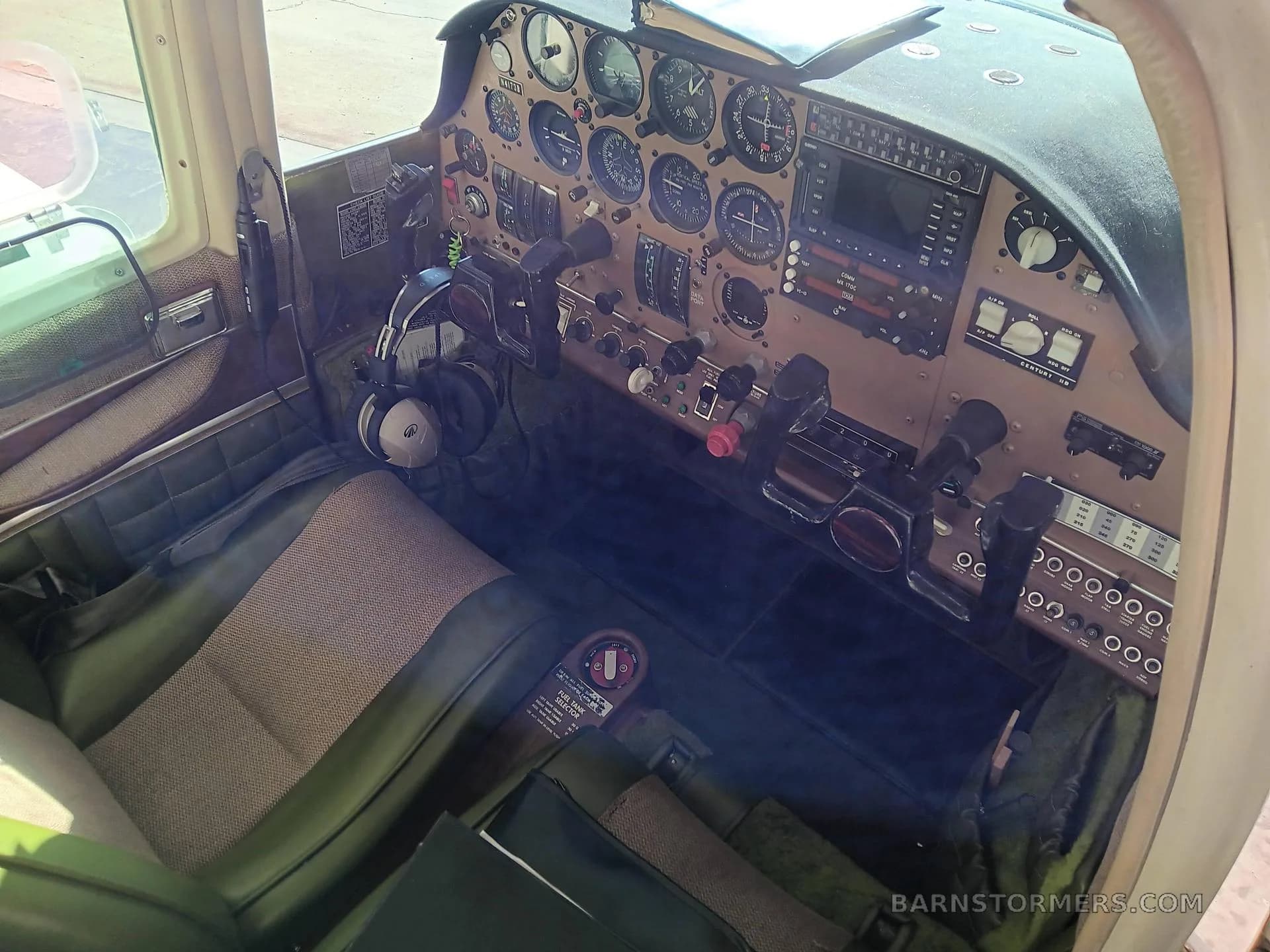 The cockpit of the aircraft, showing the instrument panel, controls, and front seats with green upholstery.