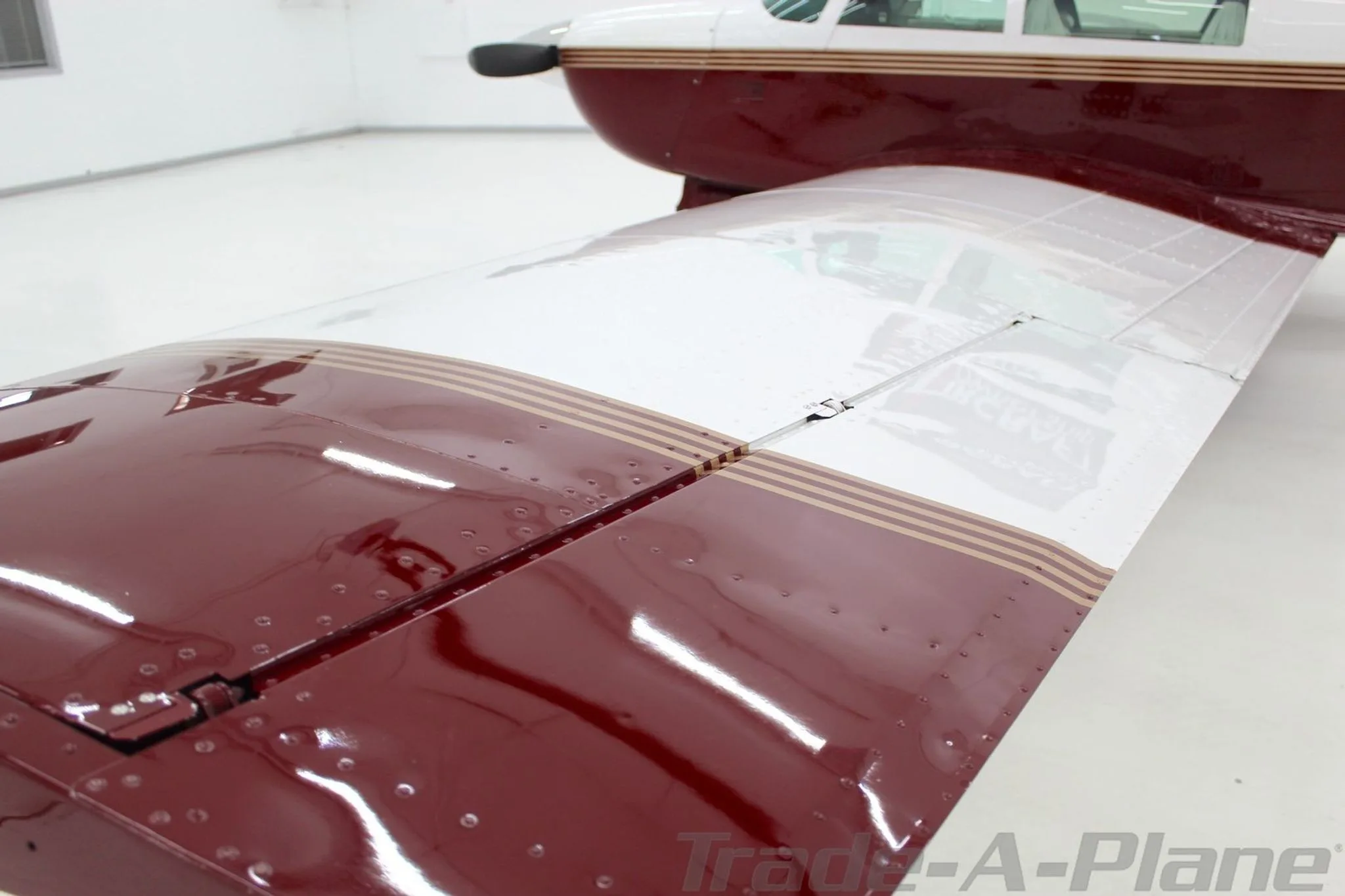 A top-down view of the Mooney M20J's wing, showing the maroon and white sections with gold stripes and rivets.