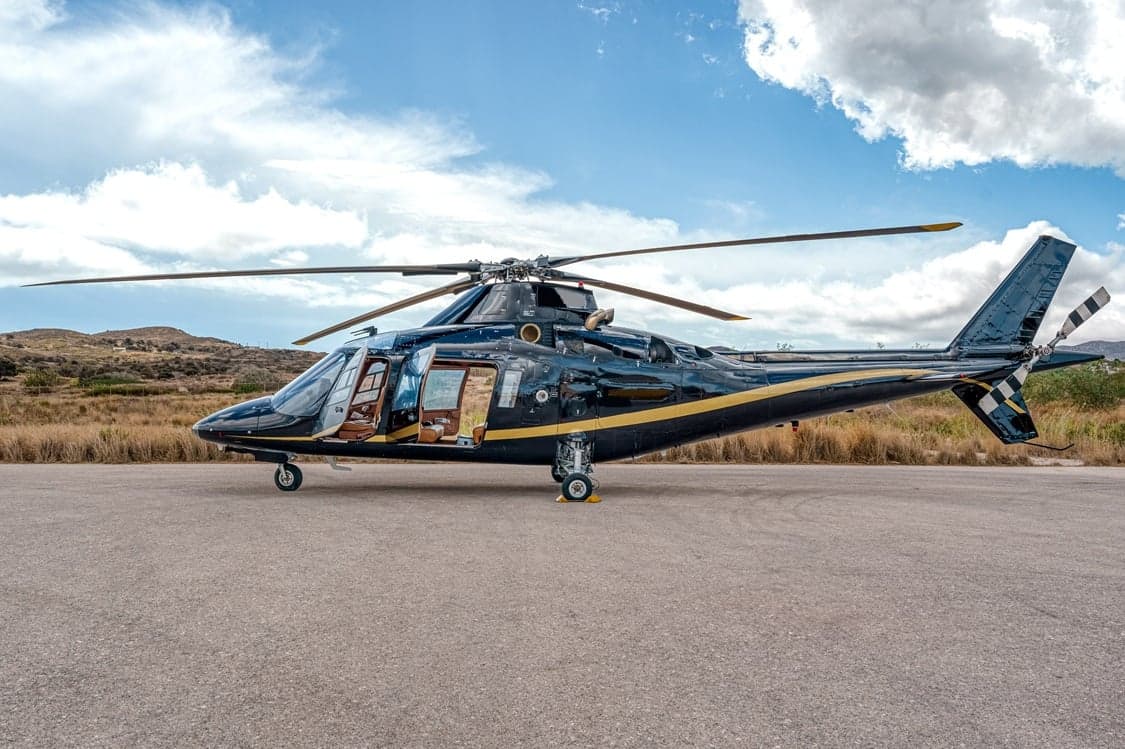 A black and gold helicopter is parked on a tarmac with its door open.