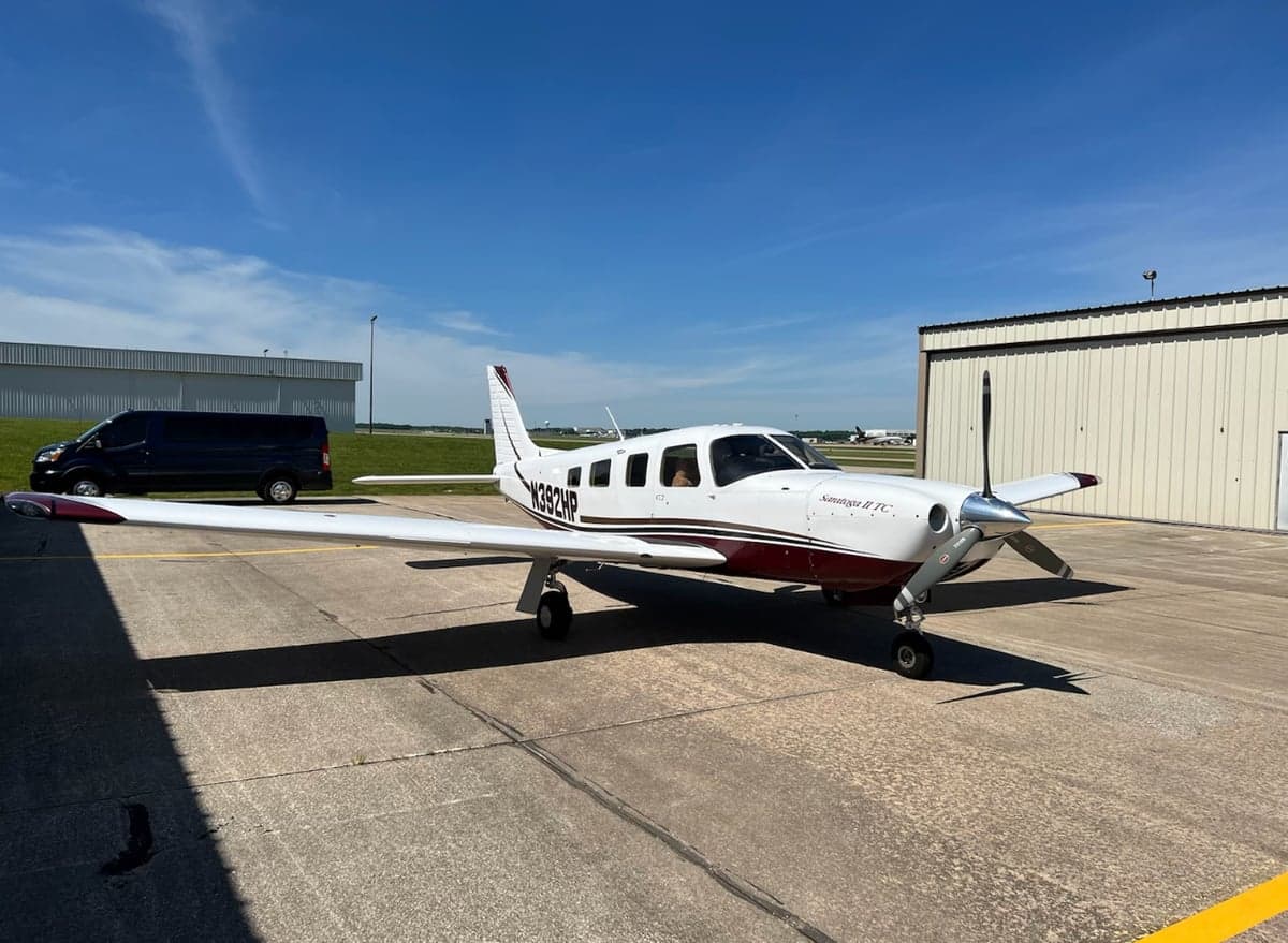 A white and maroon Piper Saratoga II TC with registration N392HP is parked on an airport tarmac on a sunny day.