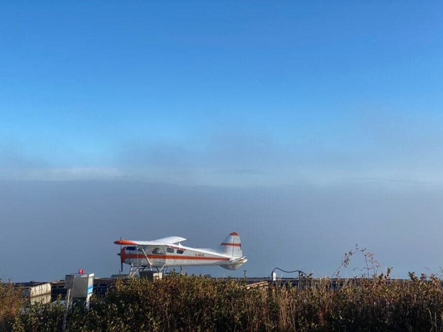 A de Havilland Beaver floatplane is docked on a wooden platform on a lake under a clear sky.