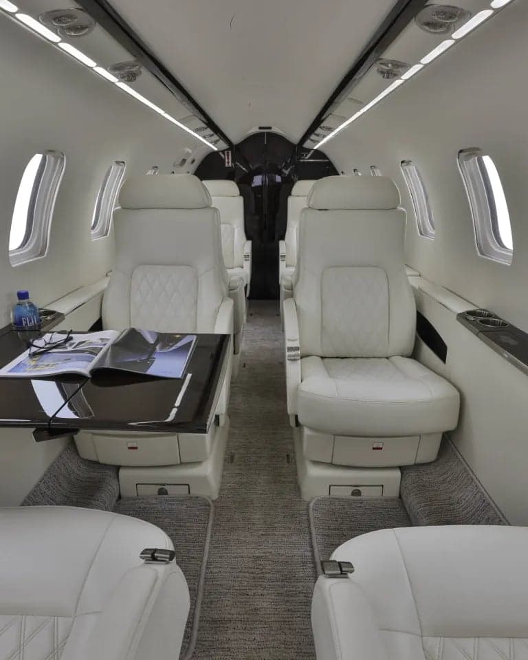 Full view of the aircraft interior with white leather seats and a dark wood table.