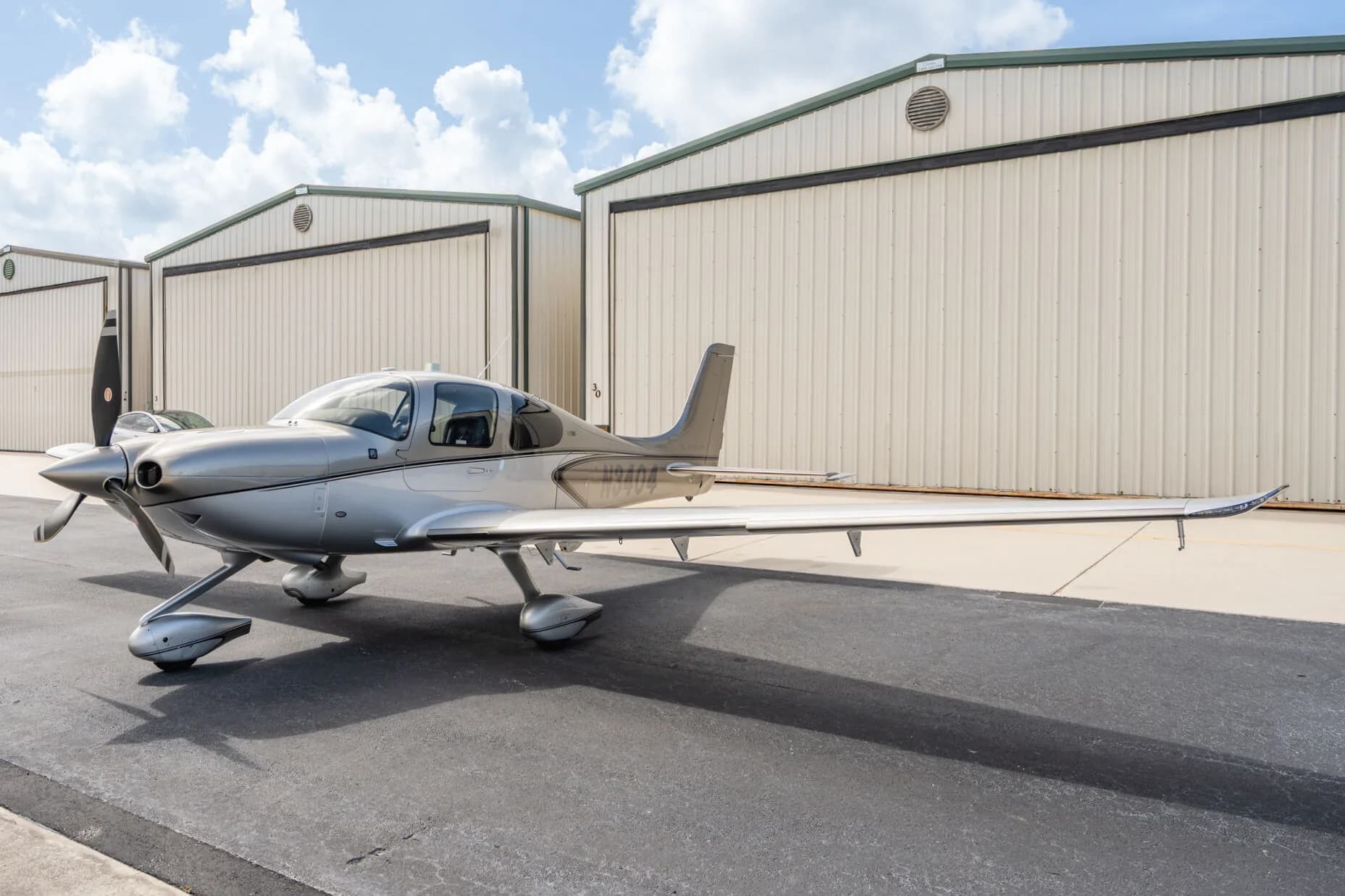 Side view of a silver Cirrus SR22T aircraft (N3404) parked on an airport tarmac under a blue sky.