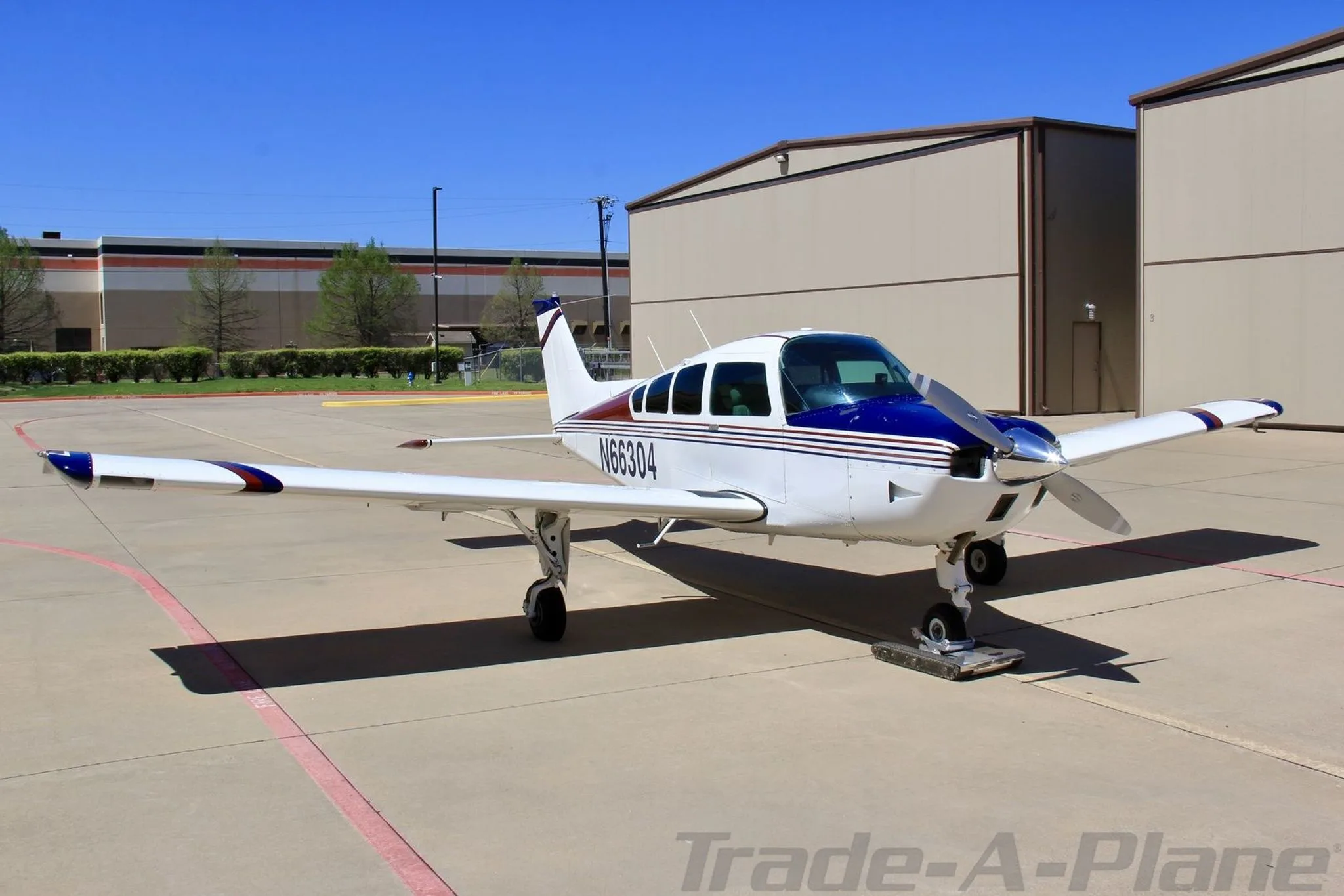 A three-quarter front view of the white, blue, and red single-engine aircraft N66304 parked on an apron.