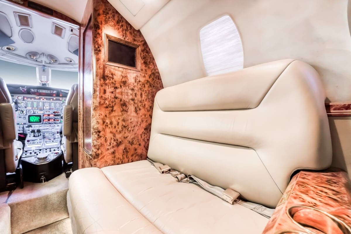 A view of the aircraft interior shows a leather seat and wood paneling, with the cockpit visible in the background.