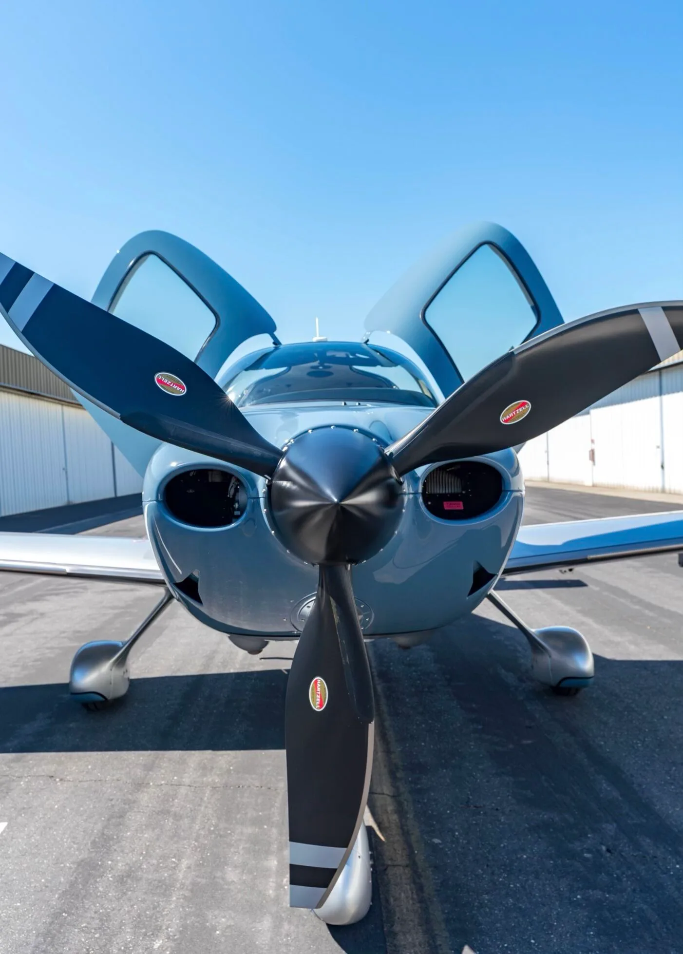 Front view of a light blue and silver Cirrus SR22T aircraft, N1383Z, with its doors open, parked on an tarmac.