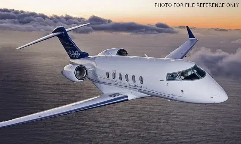 A Challenger 350 aircraft is shown in flight over the ocean at sunset.