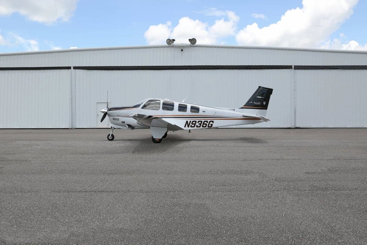 Side view of a Beechcraft Bonanza aircraft with tail number N936G parked in front of a hangar.