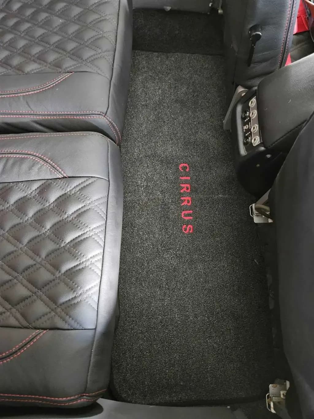 A dark grey floor mat with "CIRRUS" embroidered in red, between two black leather aircraft seats.