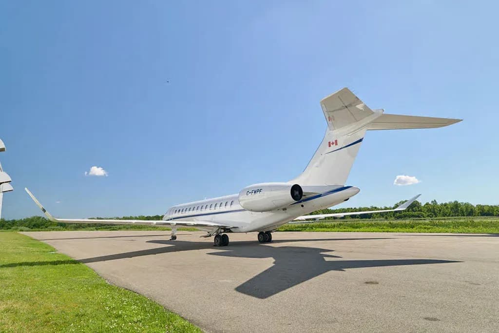 Rear view of a white Bombardier Global business jet with blue stripes on the tarmac under a clear blue sky.