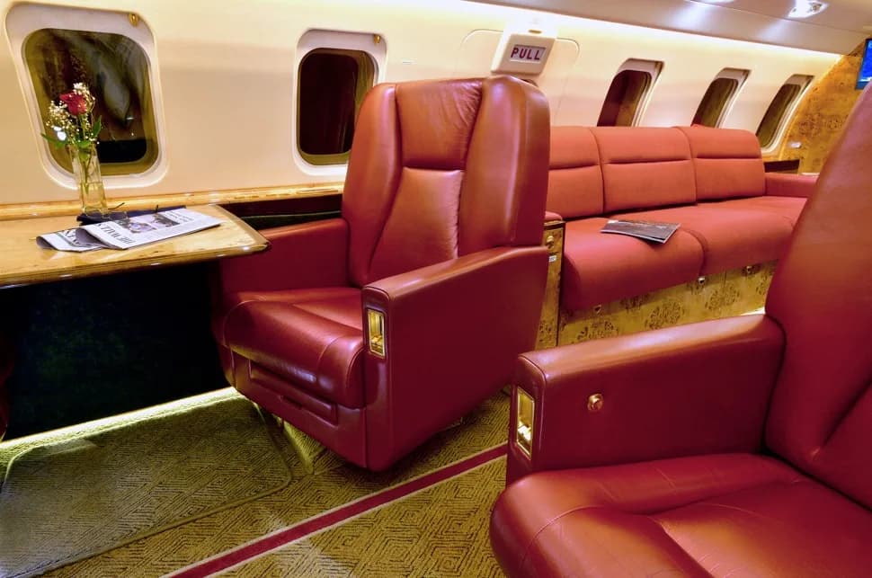 A close-up view inside the aircraft cabin showing red leather seats, a small table with a rose, and windows.