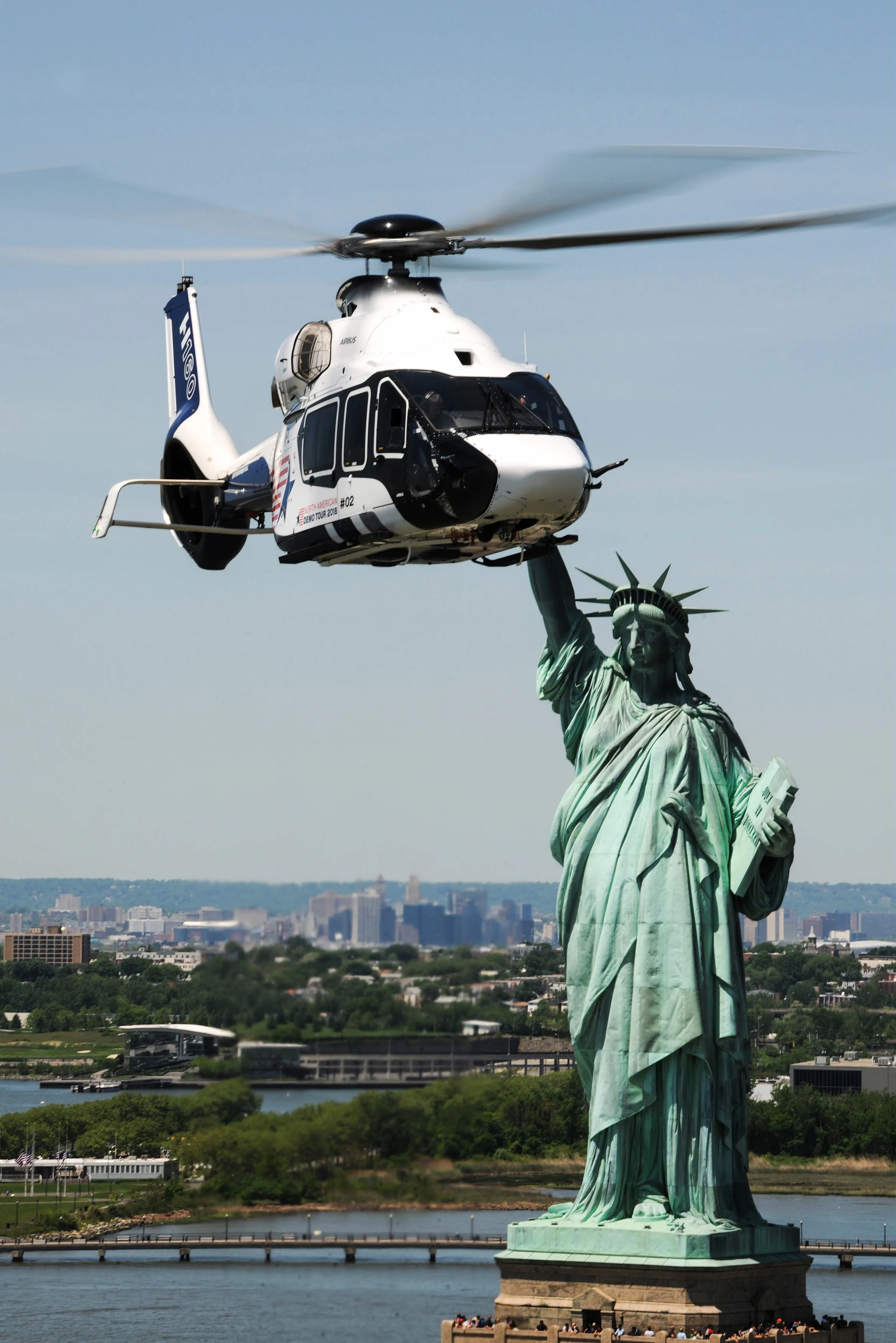 An Airbus H160 helicopter flying near the Statue of Liberty.