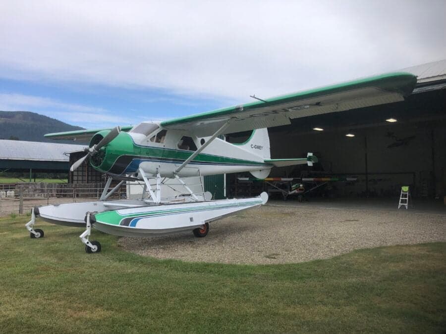 Side view of a green and white float plane parked in front of a hangar.