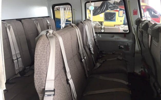 The interior cabin of a helicopter showing brown fabric passenger seats with seatbelts, looking towards the rear.