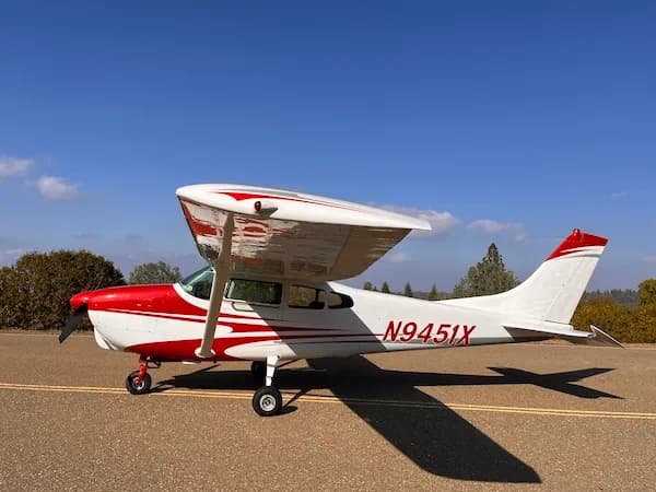 A white and red high-wing single-engine aircraft, N9451X, parked on an asphalt surface under a clear blue sky.