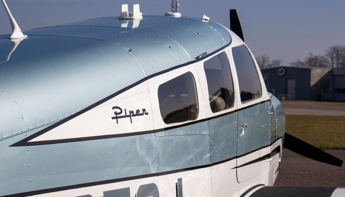 Close-up of the side of a Piper Archer II aircraft, showing the Piper logo and windows.