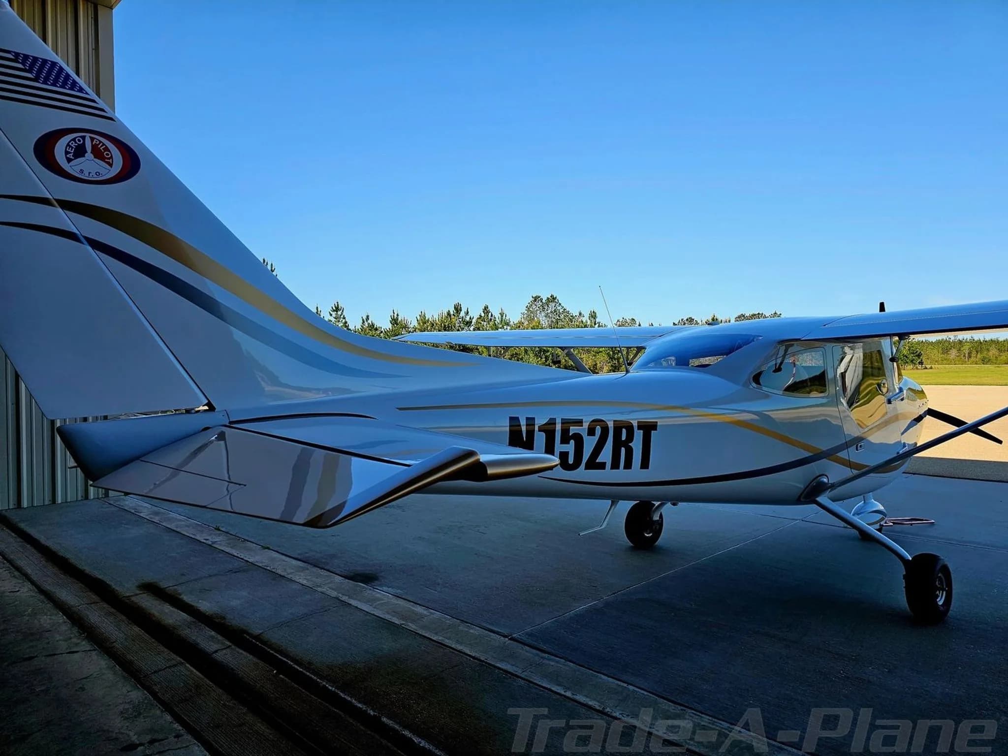 A white and gold I600 aircraft (N152RT) parked outside a hangar, viewed from the rear-left.