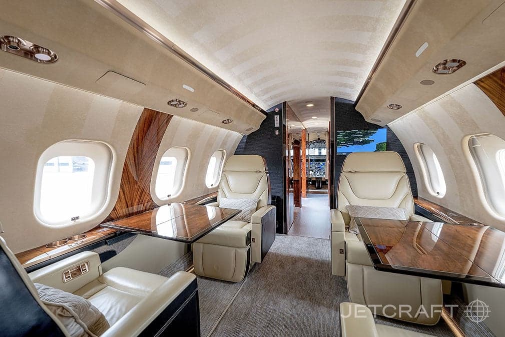 View of the aircraft cabin with tan leather seats and wood trim, with tables extended.