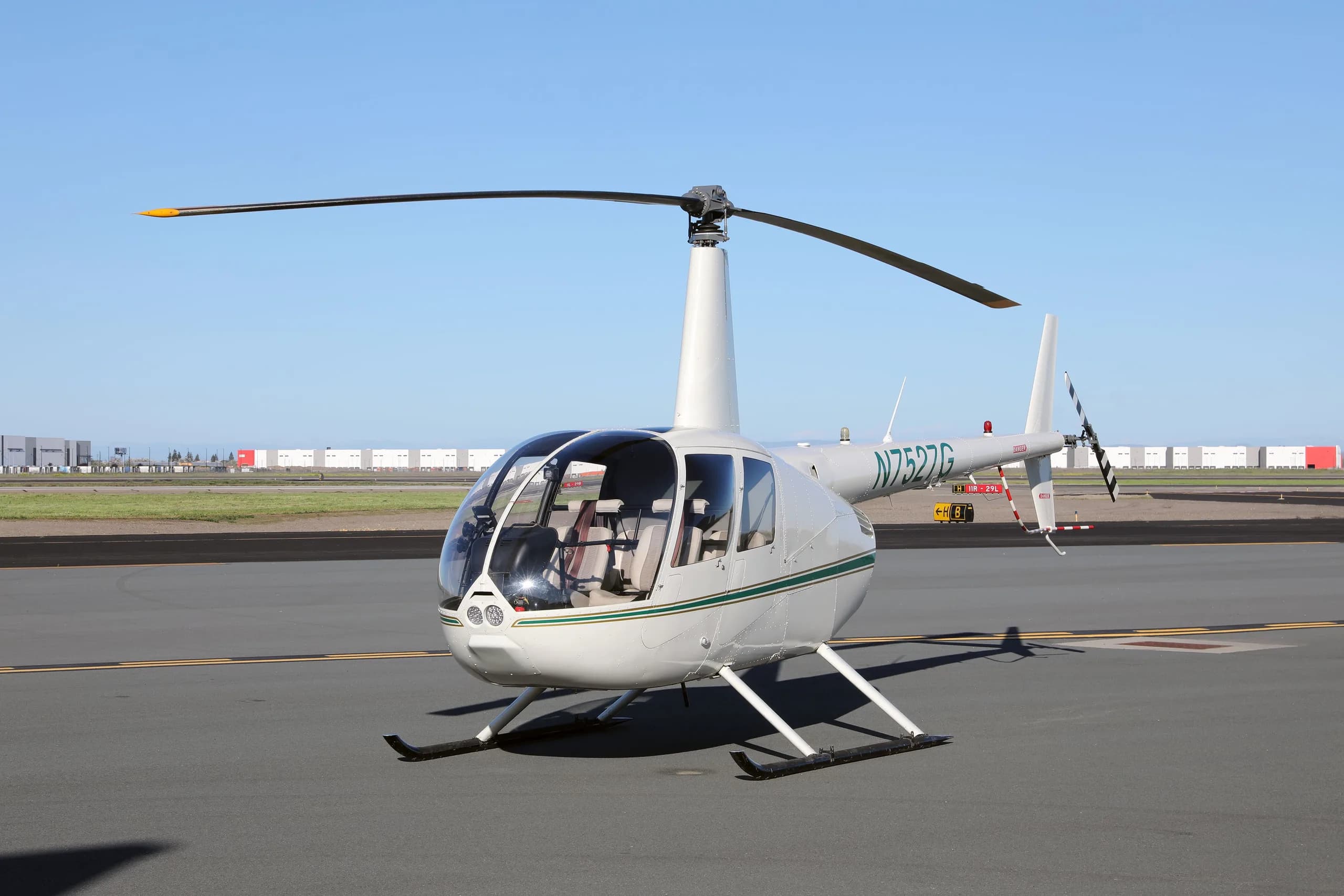 White Robinson R44 Raven II helicopter with a green stripe, registration N7527G, parked on an airfield.
