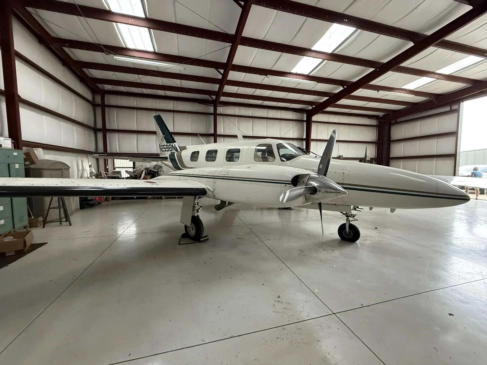 A white twin-engine Piper Navajo aircraft with green and brown stripes, seen from the front-left in a hangar.