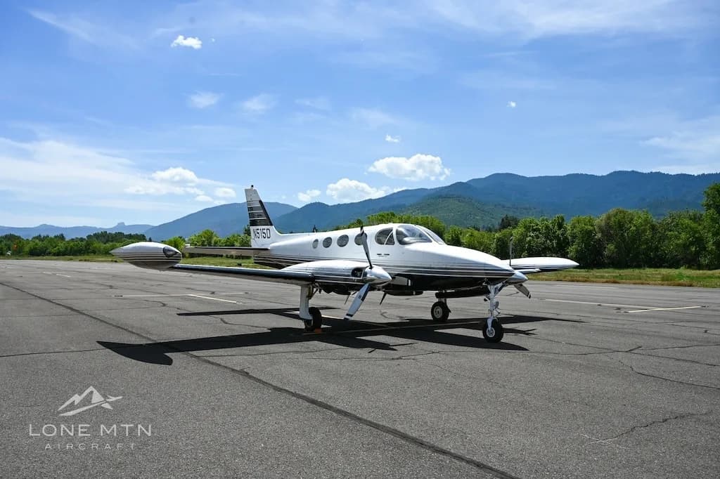 A white and black twin-engine aircraft, N515D, parked on an asphalt runway with mountains in the background.
